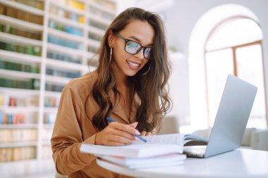 Modern kafede otururken kablosuz kulaklıklar ve dizüstü bilgisayarla çalışan serbest çalışan birinin portresi. Mutlu genç bir kadın laptopla birlikte çalışma alanında dinleniyor. Eğitim konsepti. İş, çevrimiçi.