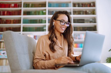 Modern kafede otururken kablosuz kulaklıklar ve dizüstü bilgisayarla çalışan serbest çalışan birinin portresi. Mutlu genç bir kadın laptopla birlikte çalışma alanında dinleniyor. Eğitim konsepti. İş, çevrimiçi.