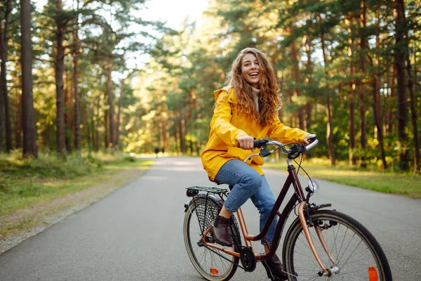 Sarı Montlu Mutlu Genç Bir Kadın Güneşli Bir Parkta Bisiklet — Stok fotoğraf
