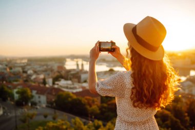 Turist kadın, şafak vakti akıllı bir telefonla şehir manzarasını vuruyor. Avrupa 'ya seyahat. Genç bir kadın güneşin doğuşunu sever. Seyahat, turizm, tatil ve özgürlük kavramı.