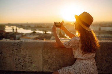 Turist kadın, şafak vakti akıllı bir telefonla şehir manzarasını vuruyor. Avrupa 'ya seyahat. Genç bir kadın güneşin doğuşunu sever. Seyahat, turizm, tatil ve özgürlük kavramı.