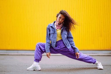 Amerikan bandanalı şık kıyafetler içinde sokakta havalı bir dansçı. Genç dansçı kadın birkaç hareket gösteriyor. Spor, dans ve şehir kültürü konsepti.