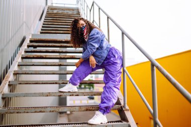 Amerikan bandanalı şık kıyafetler içinde sokakta havalı bir dansçı. Genç dansçı kadın birkaç hareket gösteriyor. Spor, dans ve şehir kültürü konsepti.