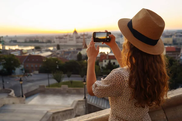 stock image Tourist woman shoots a city landscape at dawn on a smartphone. Travel in Europe. A young woman enjoys the sunrise. The concept of travel, tourism, vacation and freedom.