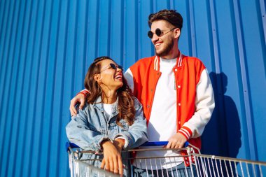 Güzel arkadaşlar açık havada alışveriş arabalarında eğleniyorlar. Yaşam tarzı, eğlence, eğlence, gençlik kavramı. Tarz sahibi erkek ve kadın eğleniyor..