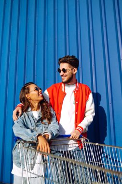 Güzel arkadaşlar açık havada alışveriş arabalarında eğleniyorlar. Yaşam tarzı, eğlence, eğlence, gençlik kavramı. Tarz sahibi erkek ve kadın eğleniyor..