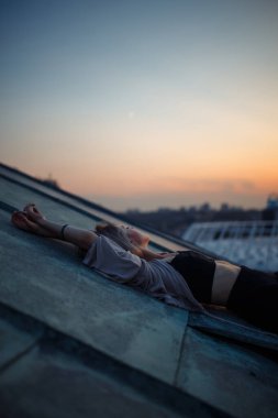 Gün batımında çatıda poz veren güzel bir kadın. Genç bir kadın özgürlük şehrinin atmosferinin tadını çıkarıyor. Rahatlama konsepti, insanlar, yaşam tarzı.