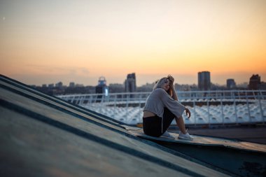 Gün batımında çatıda poz veren güzel bir kadın. Genç bir kadın özgürlük şehrinin atmosferinin tadını çıkarıyor. Rahatlama konsepti, insanlar, yaşam tarzı.