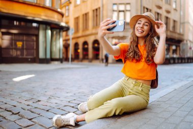 Cep telefonu tutan mutlu kadın akıllı telefon kamerasıyla selfie çekiyor. Bir turist caddelerde yürüyor ve şehrin mimarisinden zevk alıyor, manzaranın resimlerini çekiyor. Selfie zamanı.. 