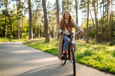 Kıvırcık saçlı gülümseyen kadın güneşli bir parkta bisiklet sürüyor. Açık hava portresi. Güzel bir kadın doğayı sever. Yaşam tarzı. Rahatla, doğa kavramı.. 