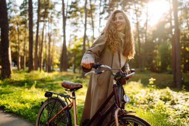 Kıvırcık saçlı gülümseyen kadın güneşli bir parkta bisiklet sürüyor. Açık hava portresi. Güzel bir kadın doğayı sever. Yaşam tarzı. Rahatla, doğa kavramı.. 