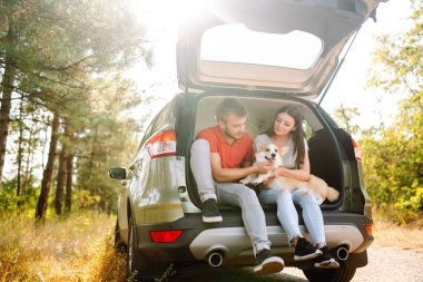 Köpekli sevimli genç bir çift arabanın arka koltuğunda oturuyor. Bir kadınla ve sevgili köpeğiyle seyahat eden mutlu bir adam. Aktif yaşam tarzı kavramı, seyahat, hafta sonu, rahatlama.