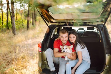 Köpekli sevimli genç bir çift arabanın arka koltuğunda oturuyor. Bir kadınla ve sevgili köpeğiyle seyahat eden mutlu bir adam. Aktif yaşam tarzı kavramı, seyahat, hafta sonu, rahatlama.