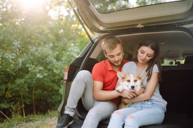 Köpekli sevimli genç bir çift arabanın arka koltuğunda oturuyor. Bir kadınla ve sevgili köpeğiyle seyahat eden mutlu bir adam. Aktif yaşam tarzı kavramı, seyahat, hafta sonu, rahatlama.