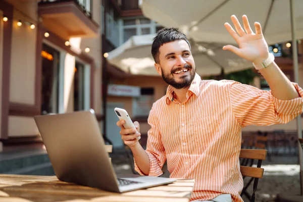 stock image Smiling young man working in a cafe on the street with a laptop and phone. Freelance business concept. Business, blogging, freelancing, education concept. Modern lifestyle.