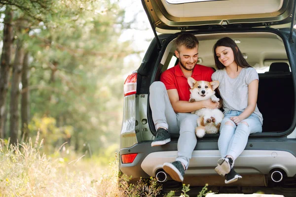 可爱的年轻夫妇带着一只狗坐在汽车后座上 一个快乐的男人与一个女人和他心爱的狗一起旅行 积极生活方式的概念 — 图库照片