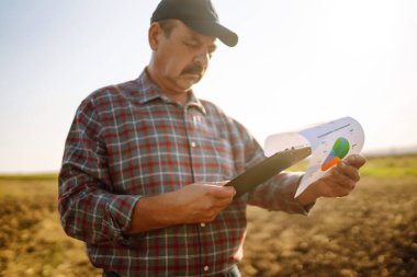 Çiftçi tarlada bir avuç toprak tutuyor. Tarlada deneyimli çiftçi, tabletle birlikte, tohum ve bitki yetiştirmeden önce toprağın kalitesini ve sağlığını kontrol ediyor. Tarım sektörü, ekoloji kavramı.