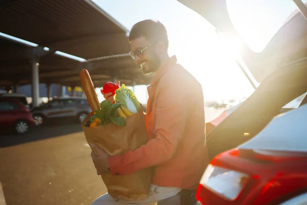 stock image Man with a cart in the parking lot with paper bags of Hungarian products. Young man with a bag near the car. The concept of a zor lifestyle, consumerism, sale, shopping.