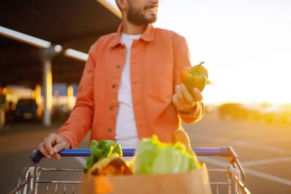 stock image Man with a cart in the parking lot with paper bags of Hungarian products. Young man with a bag near the car. The concept of a zor lifestyle, consumerism, sale, shopping.