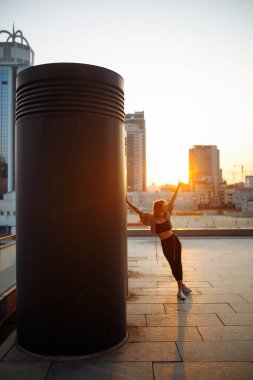 Şık bir kadın gün batımında çatıdan şehrin inanılmaz manzarasını izler. Çatıda poz veren genç bir kadın. Tarz, moda veya özgürlük konsepti, yaşam tarzı..