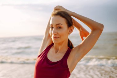 Gündoğumunda plajda yoga yapan modern genç bir kadın. Spor kadını dışarıda esneme hareketleri yapıyor. Aktif yaşam tarzı, spor eğitimi, yoga veya fitness kavramı.