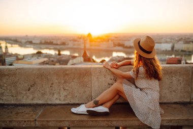 Şapkalı gülümseyen kadın turist şafak vakti şehrin manzarasına hayran kalır. Avrupa gezisi. Seyahat, turizm ve aktif yaşam tarzı konsepti.