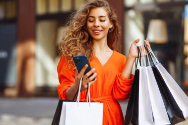 Mutlu bayan turist, güneşli Avrupa şehrinde yürürken akıllı telefon kullanarak alışveriş yapıyor. Alışveriş yaşam tarzı konsepti, tüketim.
