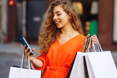 Mutlu bayan turist, güneşli Avrupa şehrinde yürürken akıllı telefon kullanarak alışveriş yapıyor. Alışveriş yaşam tarzı konsepti, tüketim.