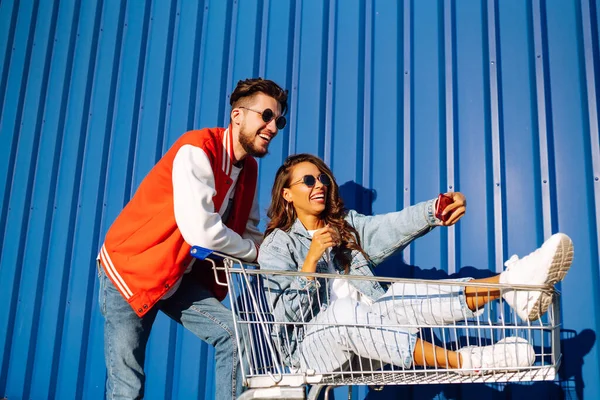 快乐的男人和女人在购物车上玩着 拿着手机 用智能手机拍着自拍 购物时间 年轻人的观念 自私的时间 — 图库照片