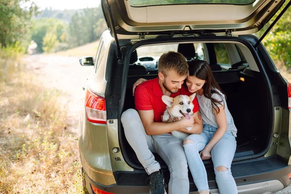 Portrait of caring and loving couple with their dog in back seat of car while traveling. Happy couple is petting their beloved corgi dog. Concept of lifestyle, vacation, travel, family.