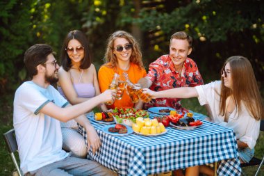 Bir grup genç arkadaş piknik için bahçede toplandı. Arkadaşlar eğlenir, doğayla iletişim kurar, bira içerler. Bölük barbekü için toplandı. Tatil kavramı, yaşam tarzı, tatil.