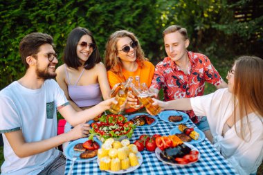 Bir grup genç arkadaş piknik için bahçede toplandı. Arkadaşlar eğlenir, doğayla iletişim kurar, bira içerler. Bölük barbekü için toplandı. Tatil kavramı, yaşam tarzı, tatil.