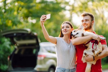 Selfie zamanı. Genç çift, sevgili hayvanlarıyla birlikte yürüyüş yapıyor. Aktif yaşam tarzı, seyahat, aşk ve tatil kavramı. Evcil hayvan ve insan.