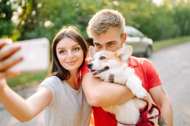 Selfie zamanı. Genç çift, sevgili hayvanlarıyla birlikte yürüyüş yapıyor. Aktif yaşam tarzı, seyahat, aşk ve tatil kavramı. Evcil hayvan ve insan.
