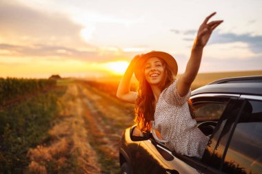 Genç bayan dinleniyor ve arabada günbatımının tadını çıkarıyor. Yaz gezisi. Yaşam tarzı, seyahat, turizm, doğa, aktif yaşam.