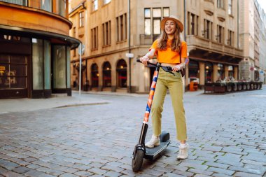 Şehirde elektrikli scooter kullanan genç bir kadın. Aktif hayat. Ekolojik ulaşım kavramı.