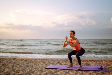 Aktif yaşam tarzı. Gün doğumunda kumsalda sabah yogası yapan genç ve güzel bir kadın, dışarıda esneme hareketleri yapıyor. Spor kavramı, spor eğitimi, yoga ya da fitness.