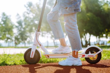 Elektrikli scooterlı genç kadın bacakları. Güneşli bir günde parkta elektrikli scooter süren güzel bir kadın. Ekolojik nakliye. Etkin yaşam biçimi.