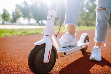 Elektrikli scooterlı genç kadın bacakları. Güneşli bir günde parkta elektrikli scooter süren güzel bir kadın. Ekolojik nakliye. Etkin yaşam biçimi.