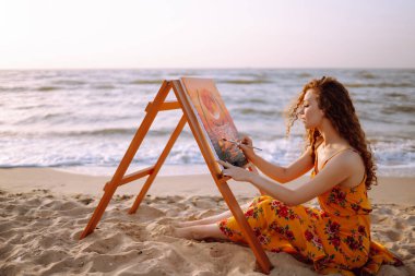 Genç bir kadın sahilde resim çiziyor. Hobi ve eğlence konsepti. Yetenek ve yaratıcılık. Tablo boyama.