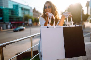 Alışveriş çantalı mutlu bir kadın güneşli bir sokakta yürüyor. Yaşam tarzı, alım, satım, tüketim kavramı.