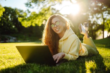 Bilgisayarlı gülümseyen genç bir kadın bir şehir binasının arka planında çalışıyor ya da çalışıyor. Eğitim, iş, blog veya serbest çalışma kavramı.