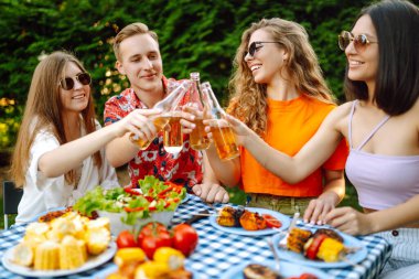 Bir grup genç arkadaş doğada bira eşliğinde piknik yapıyorlar. İnsanlar, yaşam tarzı, rahatlama ve tatil kavramı.