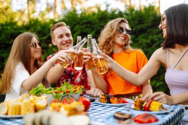 Bir grup genç arkadaş doğada bira eşliğinde piknik yapıyorlar. İnsanlar, yaşam tarzı, rahatlama ve tatil kavramı.