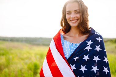Genç bir kadın çiçek açan çayırda Amerikan bayrağı sallıyor. 4 Temmuz. Bağımsızlık Günü. Vatansever bayram. 