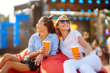İki genç kadın bira içiyor ve plaj partisinde birlikte eğleniyorlar. Müzik festivali. Yaz tatili, tatil konsepti.
