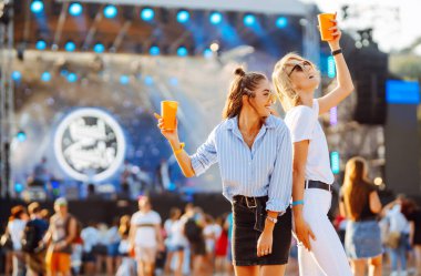 İki genç kadın bira içiyor ve plaj partisinde birlikte eğleniyorlar. Müzik festivali. Yaz tatili, tatil konsepti.