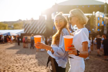 İki genç kadın bira içiyor ve plaj partisinde birlikte eğleniyorlar. Müzik festivali. Yaz tatili, tatil konsepti.