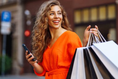 Alışveriş merkezinin yakınında alışveriş torbaları olan genç bir kadın. Yaz stili. Tüketim, satın alma, alışveriş, yaşam tarzı, satış kavramı.