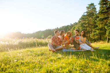 Bir grup arkadaş birlikte eğlenir ve sıcak yaz gününde karpuz yerler. İnsanlar, yaşam tarzı, seyahat, doğa ve tatil kavramı. 